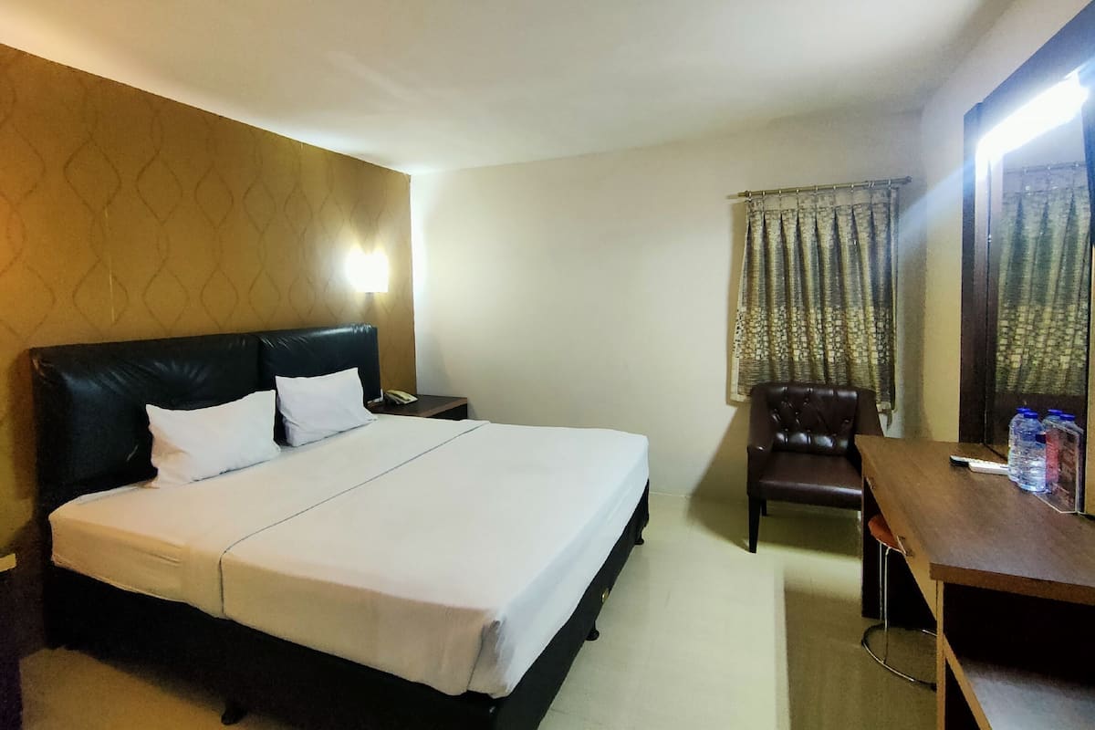 A hotel room with a large bed, a desk, a chair, and a nightstand.