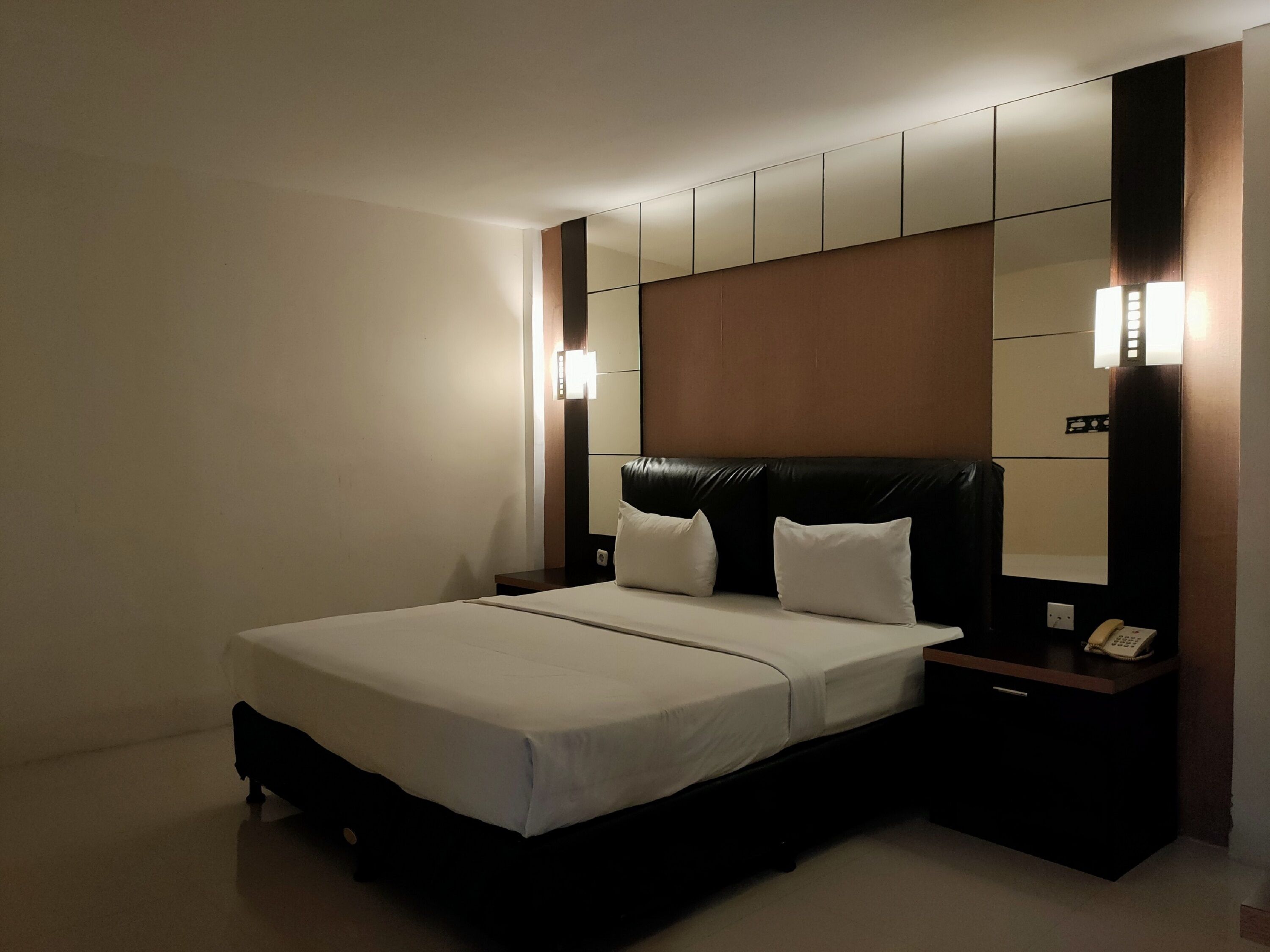A hotel room with a large bed, a nightstand with a telephone, and a wall-mounted light fixture.
