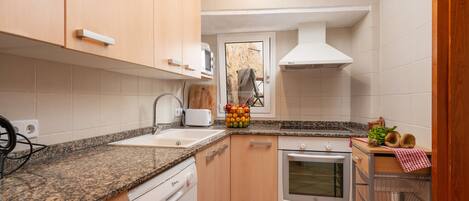A compact kitchen with a granite countertop, white cabinets, a built-in oven, and a stainless steel sink.