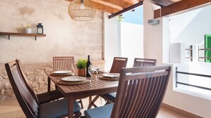 Een houten eettafel gedekt met borden, glazen en een fles, omringd door stoelen, in een kamer met een rustieke plafond en een groot raam.