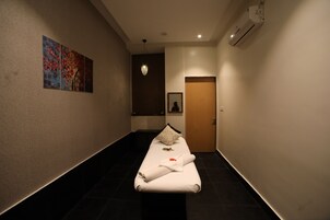 Habitación de hotel con una mesa de masaje, un cuadro en la pared, una puerta y un equipo de aire acondicionado.