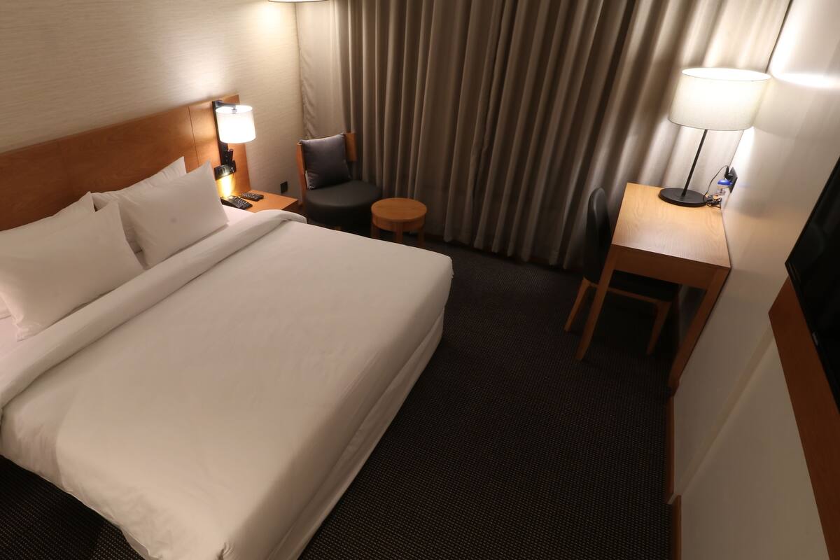 A hotel room with a large bed, a desk, a chair, and a lamp.