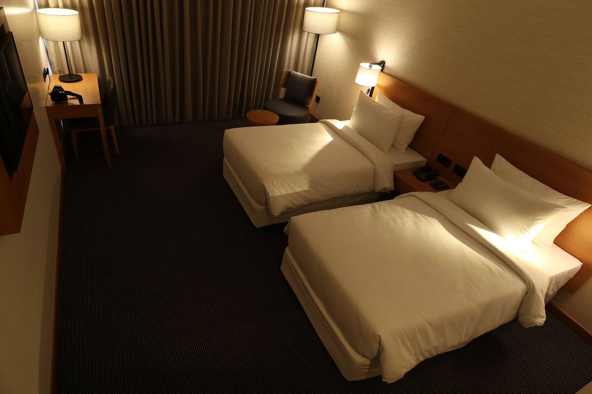 A hotel room with two beds, a desk with a lamp, a chair, and a small table.