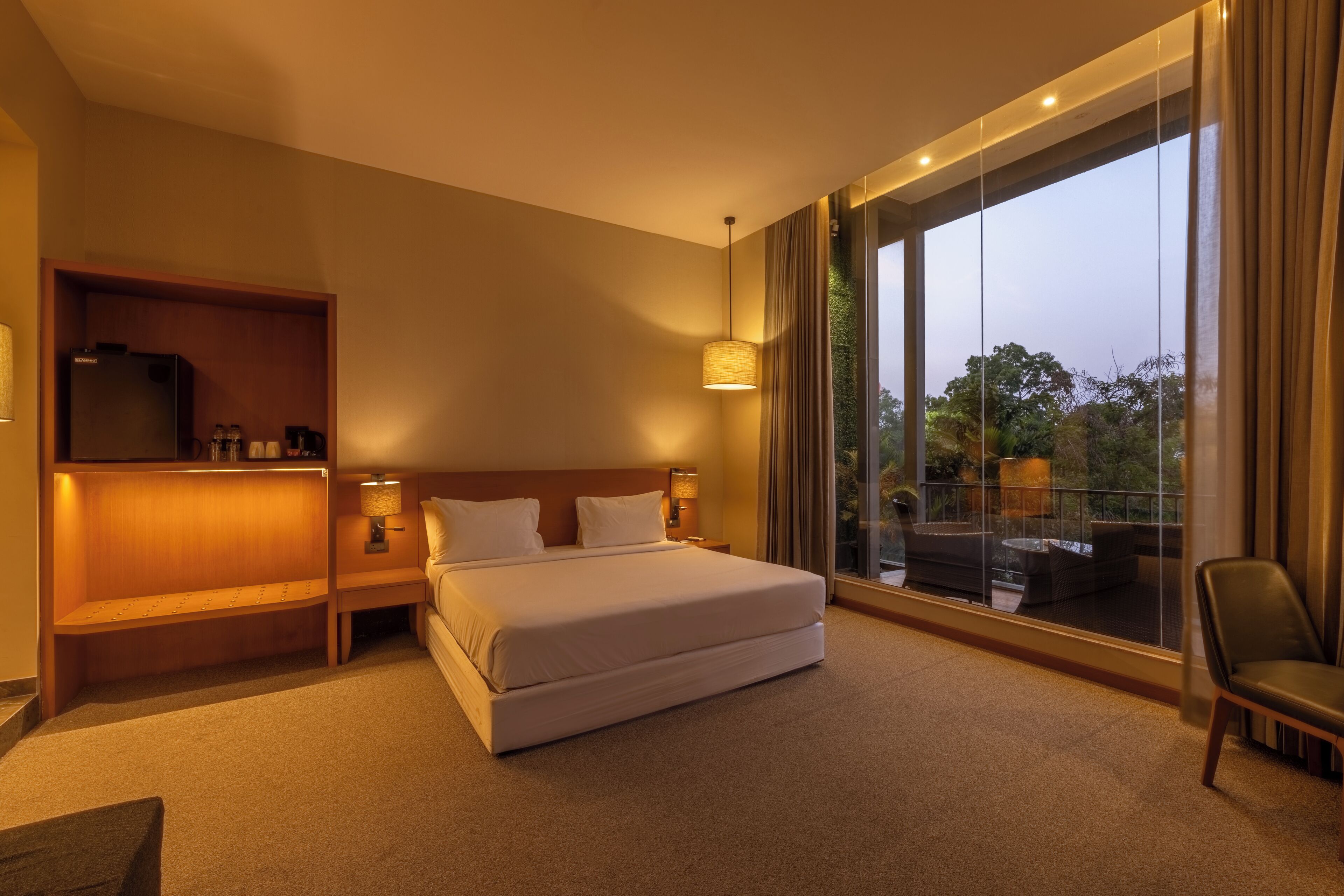 A hotel room with a large bed, a TV, a sofa, and a balcony with a view.