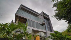 Un edificio moderno de dos pisos con grandes ventanales, un balcón y una escalera que conduce a la entrada.