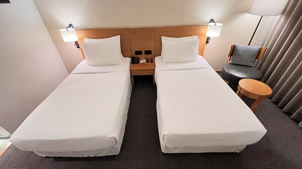 A hotel room with two single beds, a small table, a chair, and a lamp.