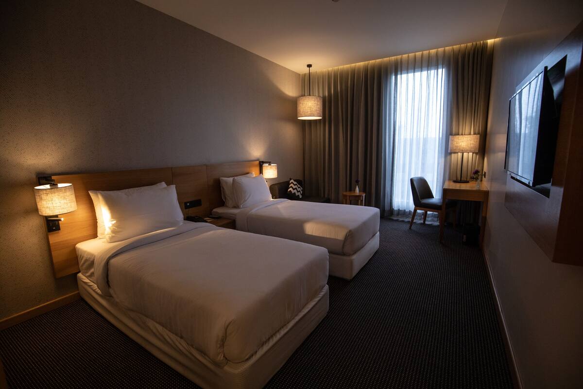 A hotel room with two beds, a desk, a chair, and a TV.