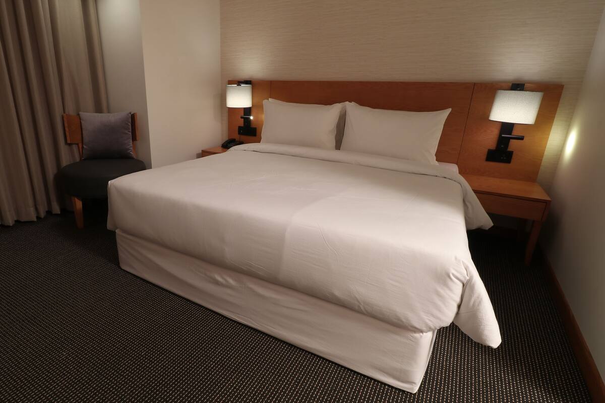 A hotel room with a large bed, two bedside tables with lamps, a chair, and a window with curtains.