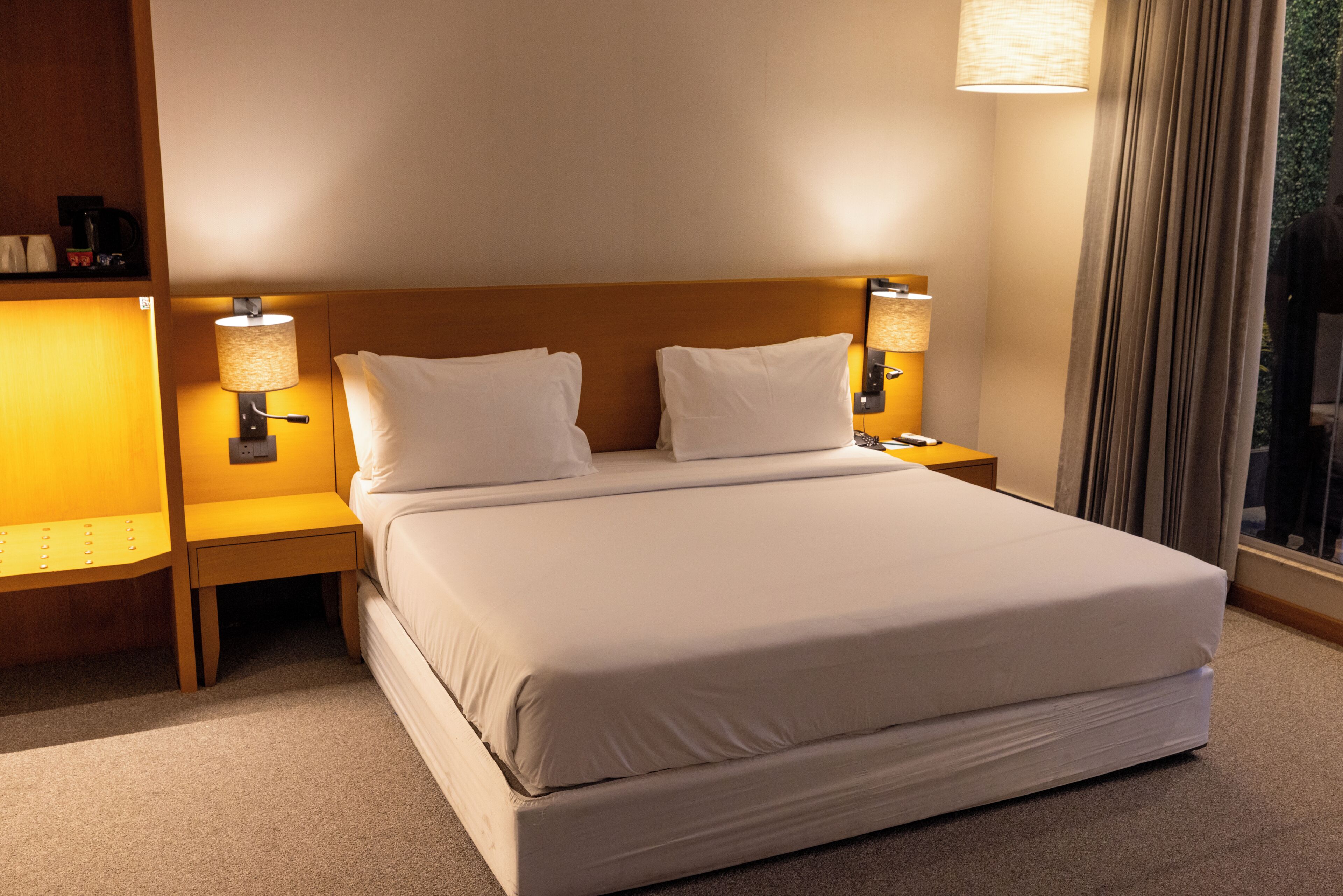 A hotel room with a large bed, two bedside lamps, a nightstand, and a window with curtains.
