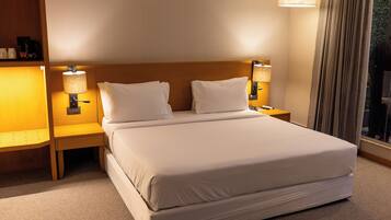 Habitación de hotel con una cama grande, dos lámparas de noche, una mesita de noche y una ventana con cortinas.