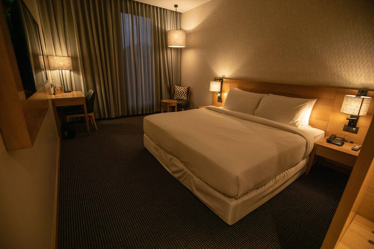 A hotel room with a large bed, a desk with a chair, a lamp, and a telephone on the nightstand.