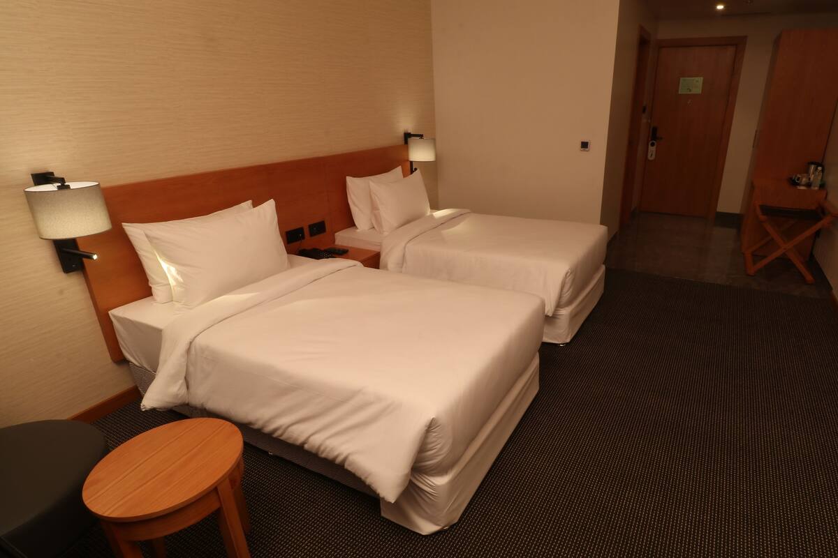 A hotel room with two beds, a small round table, and a desk with a lamp.