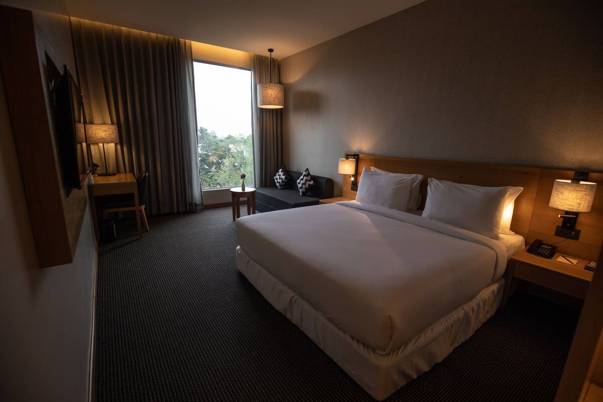 A hotel room with a large bed, bedside lamps, a desk with a lamp, a view of the outdoors, and a window with curtains.