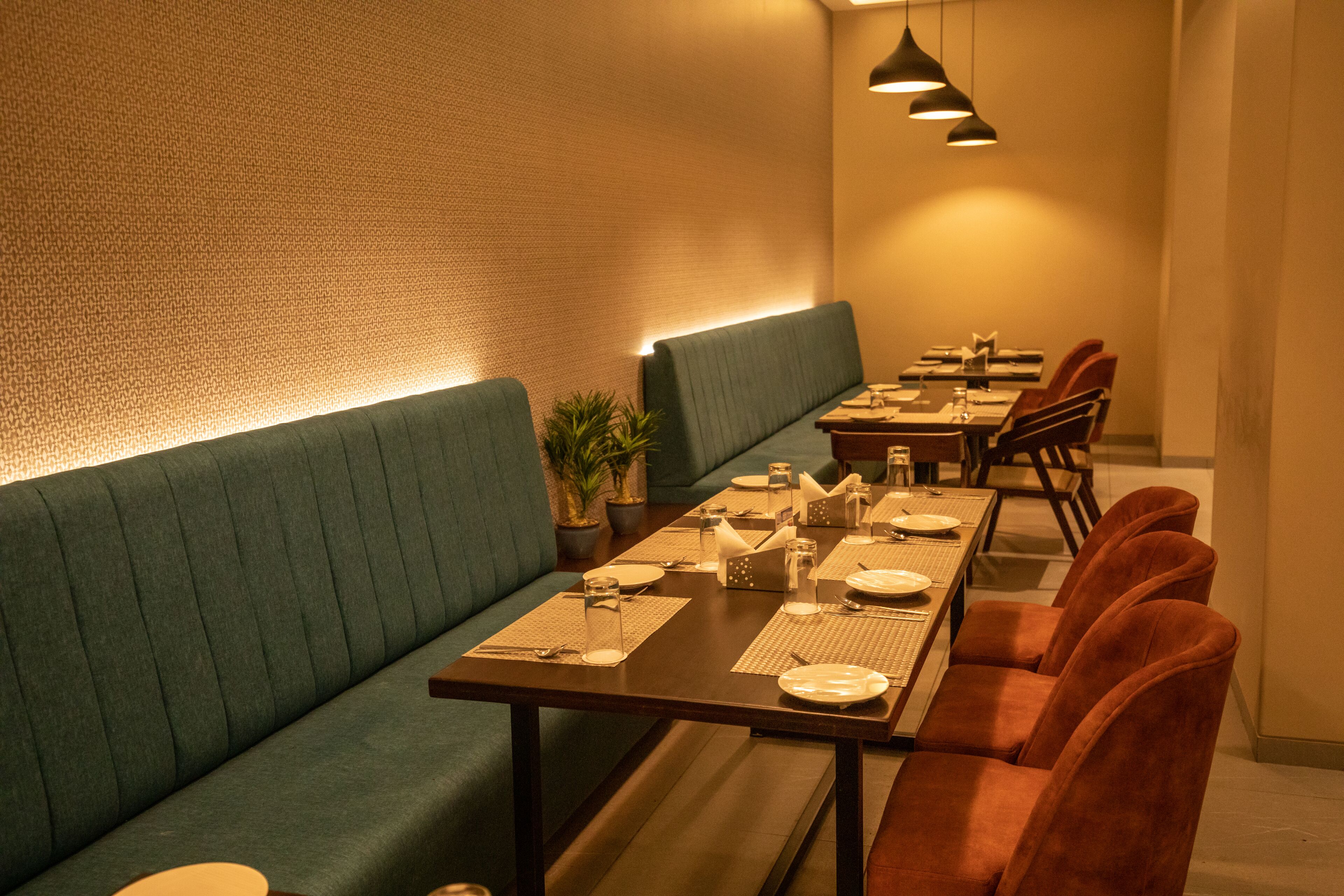 Um restaurante com uma mesa de jantar comprida, assentos acolchoados e iluminação pendente.