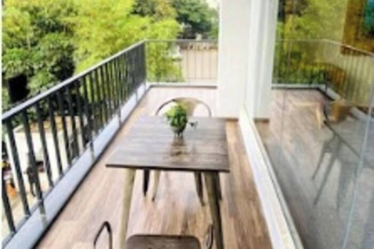 A balcony with a wooden table and chairs, a potted plant, and a view of greenery.