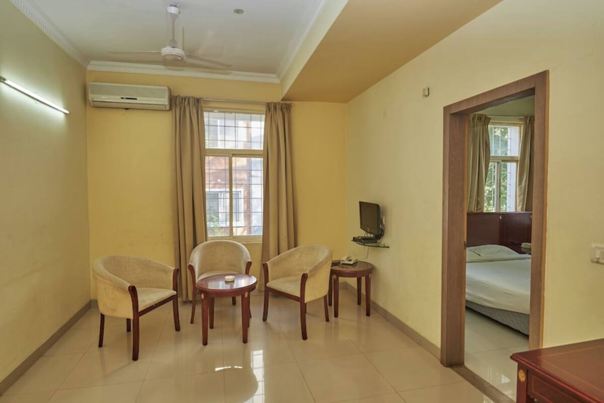A hotel room with two armchairs, a small table, a television, and a bed.