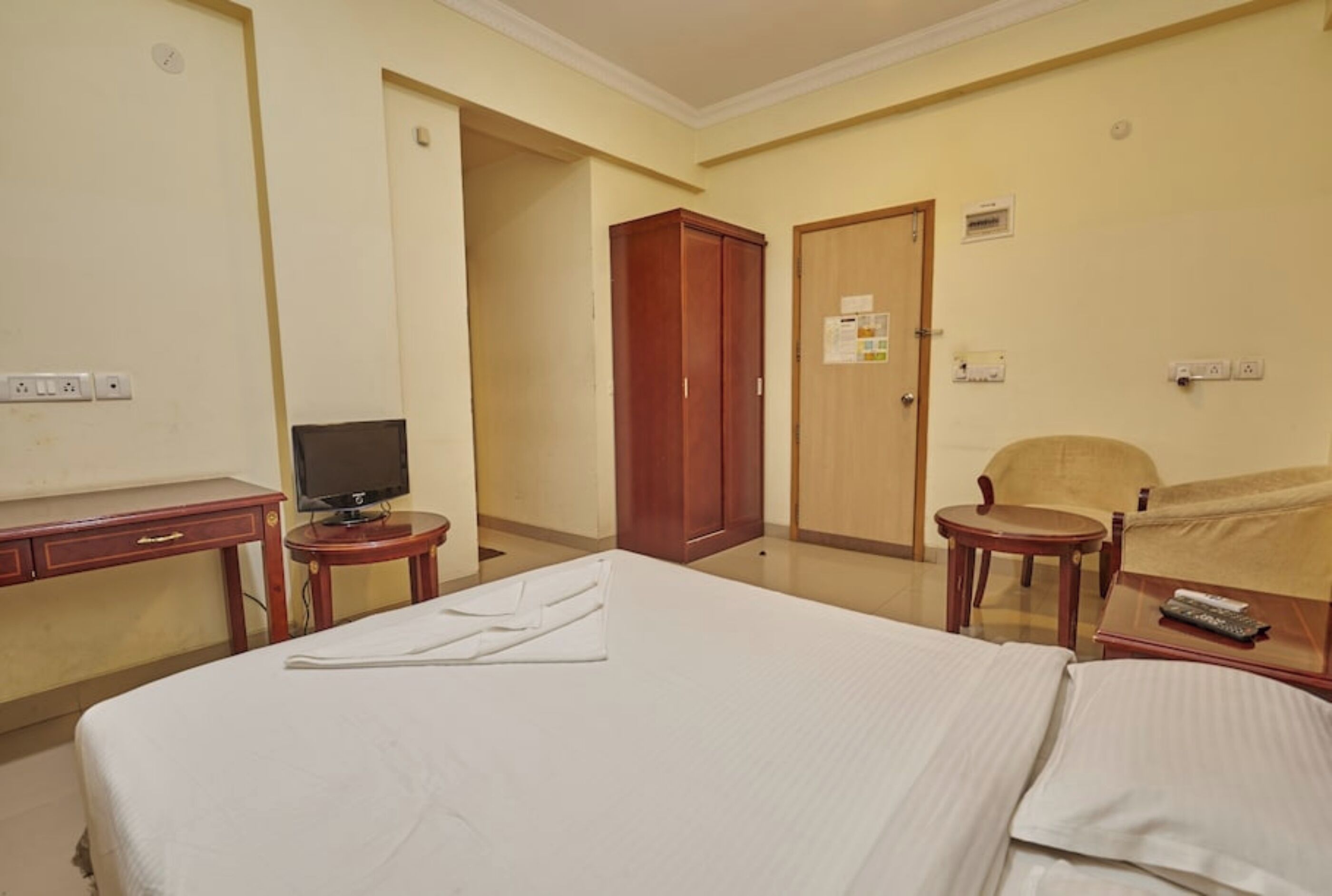 A hotel room with a bed, a desk with a television, a wardrobe, and a chair.