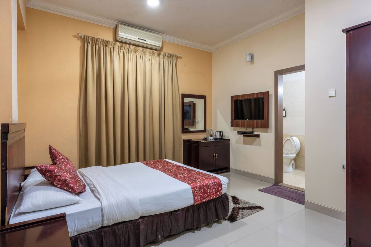 A hotel room with a bed, a wardrobe, a mirror, a television, and a bathroom visible through an open door.