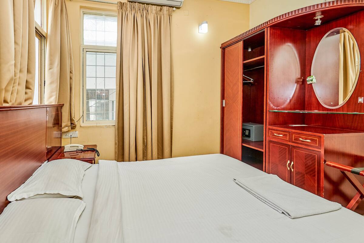 A hotel room with a bed, a wardrobe, a mirror, and a window with curtains.