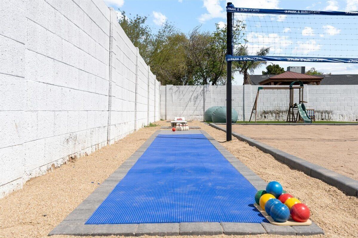 A blue mat leading to a volleyball net with a wall and a small shelter in the background.