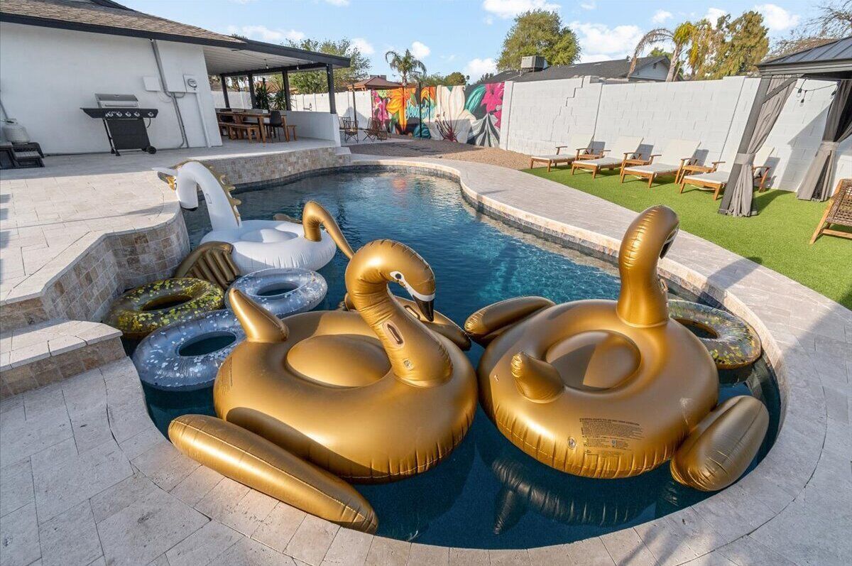 A swimming pool with gold and blue inflatable swans and a barbecue area.