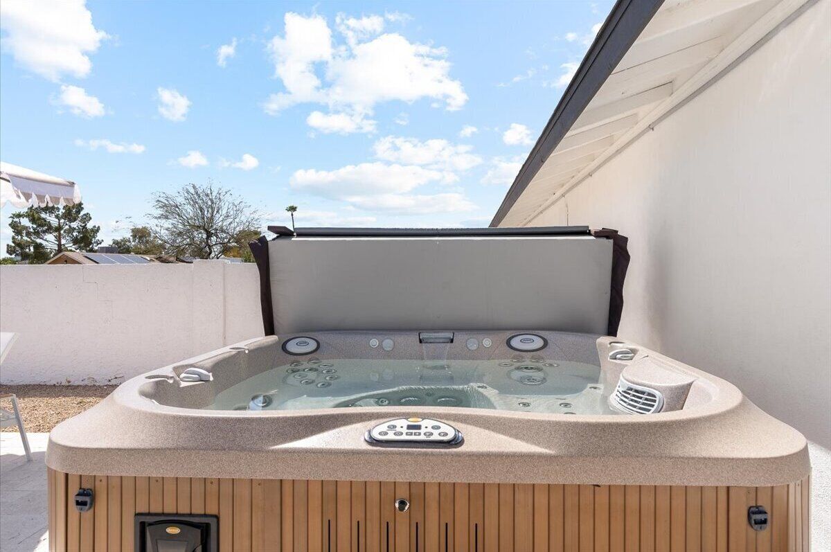A hot tub with a control panel, set against a clear sky and a white wall.