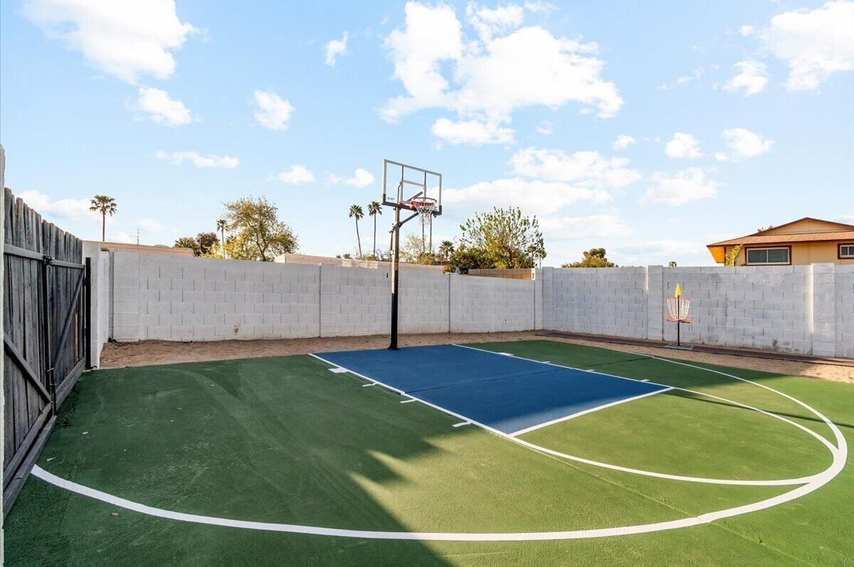 An outdoor basketball court with a hoop, surrounded by a brick wall and a wooden fence.