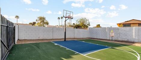 An outdoor basketball court with a hoop, surrounded by a brick wall and a wooden fence.