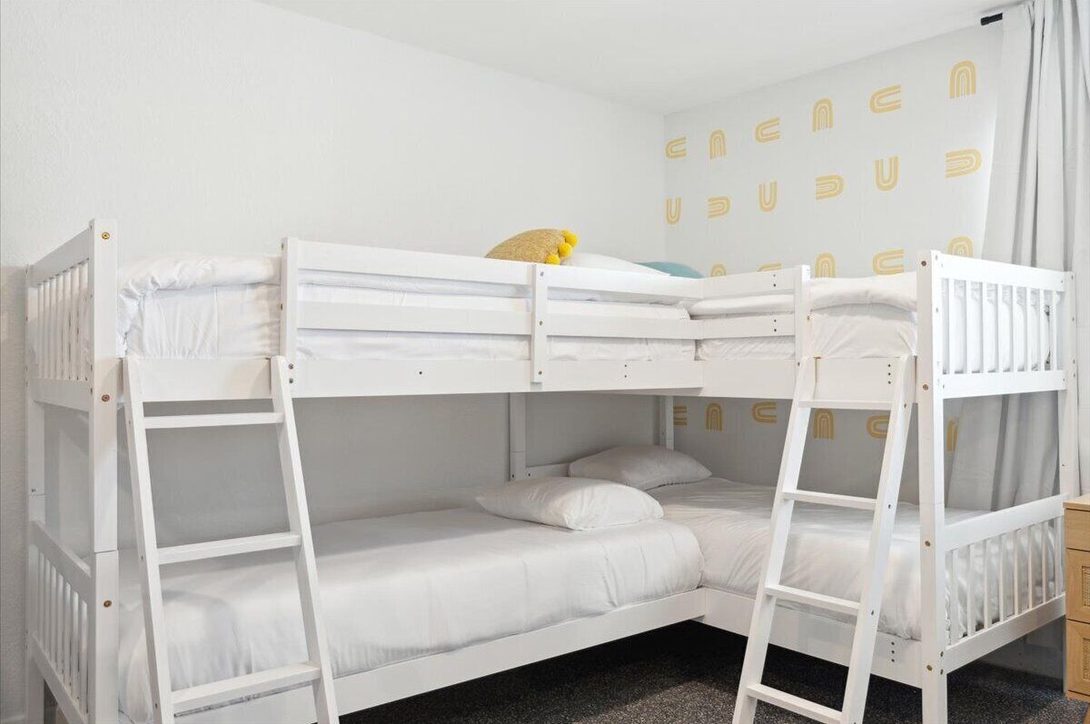 Habitación con literas, ropa de cama blanca y un juguete amarillo en la litera superior.