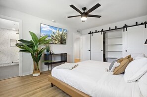 Une chambre à coucher avec un lit, un ventilateur de plafond, une télévision, une plante et un mur en briques blanches.