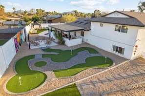 Une maison moderne dotée d’un jardin aménagé comprenant un green d’entraînement et un espace patio.