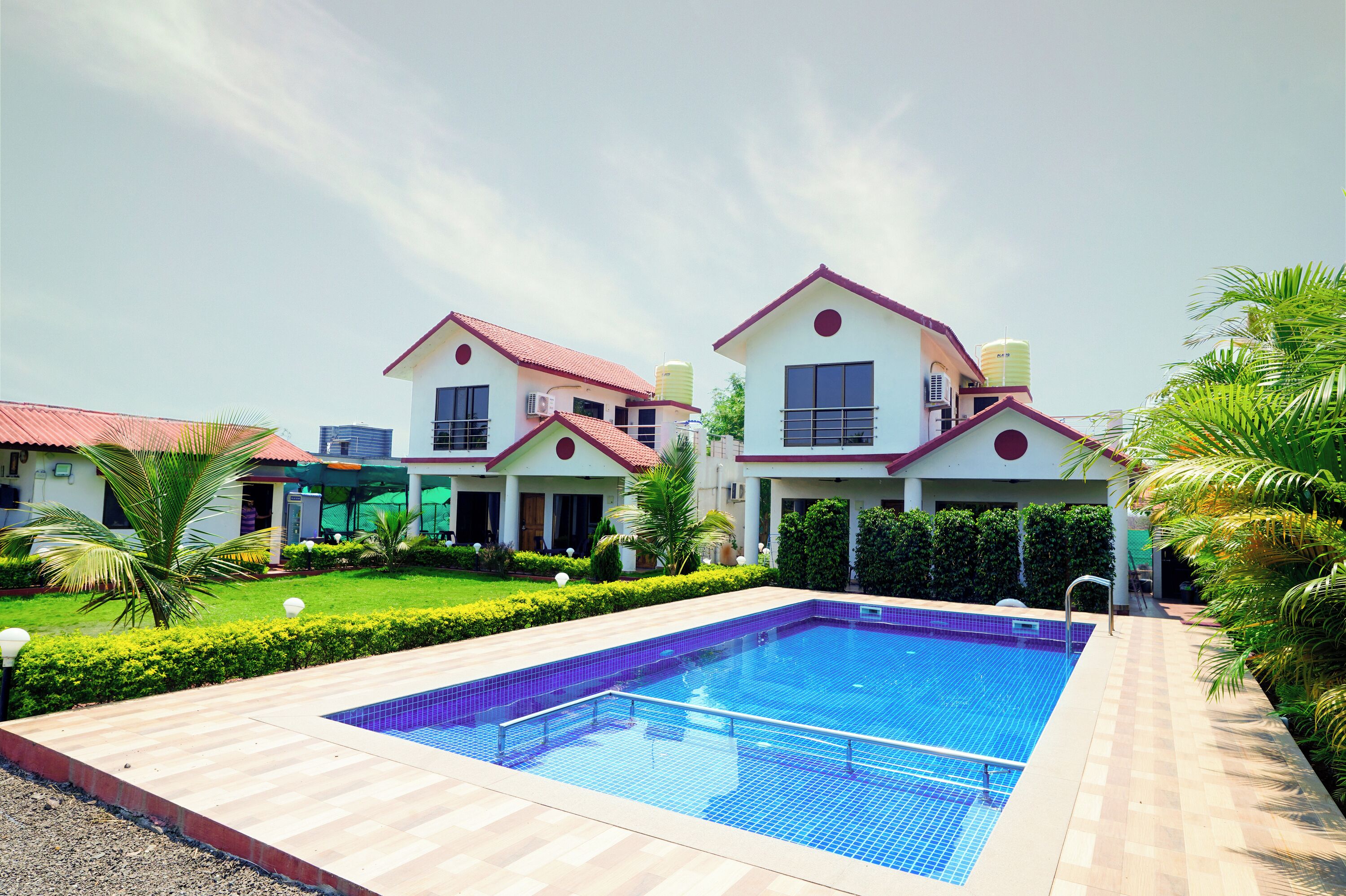 A swimming pool with a tiled deck, surrounded by manicured hedges and palm trees.