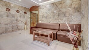 Un vestíbulo moderno con pared de mármol, sofá de cuero marrón, mesa de centro de vidrio y jarrones decorativos.
