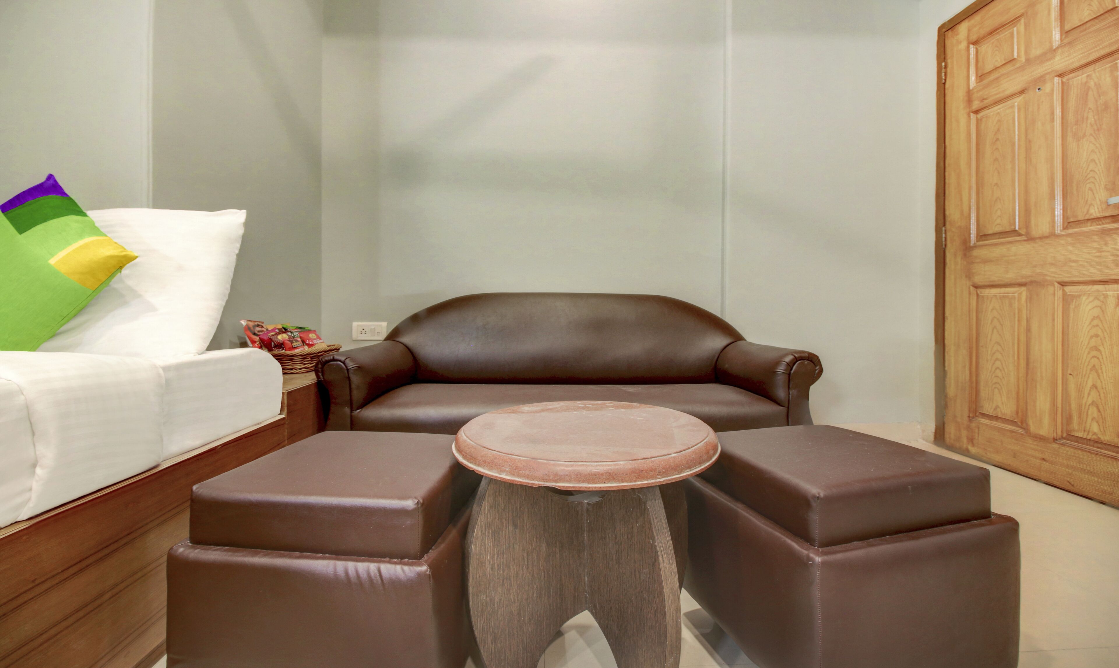 Ein Zimmer mit einer braunen Ledersofa, einem kleinen runden Holztisch und einem weißen Bett mit Kissen.