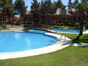 Relax by the pool surrounded by lush greenery and a wooden bridge.