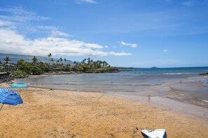 A beach with umbrellas, a boat, and a view of the ocean and mountains.