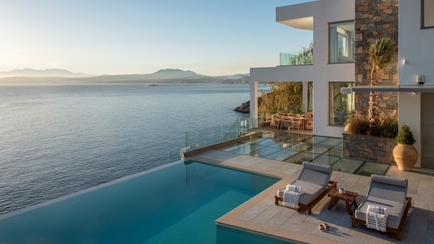 Une maison moderne dotée d’une piscine à débordement en verre, offrant une vue imprenable sur une mer calme.