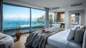 Une chambre moderne avec une grande fenêtre, un lit, une table de chevet et une vue sur la mer.
