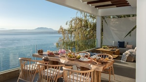 Un coin repas avec vue sur la mer, des meubles en bois et une table dressée avec de la nourriture et des boissons.