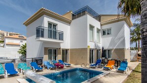 Un hotel moderno con piscina, tumbonas y un área de estar cubierta al aire libre.