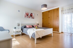 Une chambre à coucher comprenant un lit, des tables de chevet, une commode, une armoire et une fenêtre avec des rideaux.