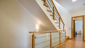 Un interior moderno con escalera de madera, barandilla de vidrio y un pasillo que conduce a otra habitación.