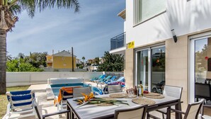 Zona de piscina al aire libre con sillas de descanso, una mesa de comedor con individuales y una vista despejada del vecindario circundante.