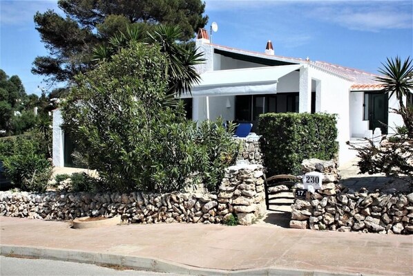A white building with a stone wall, a stone pillar, and a blue chair outside.
