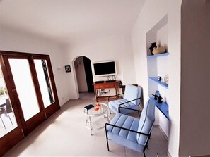 A living room with a TV, two blue chairs, a small table, and a bookshelf.