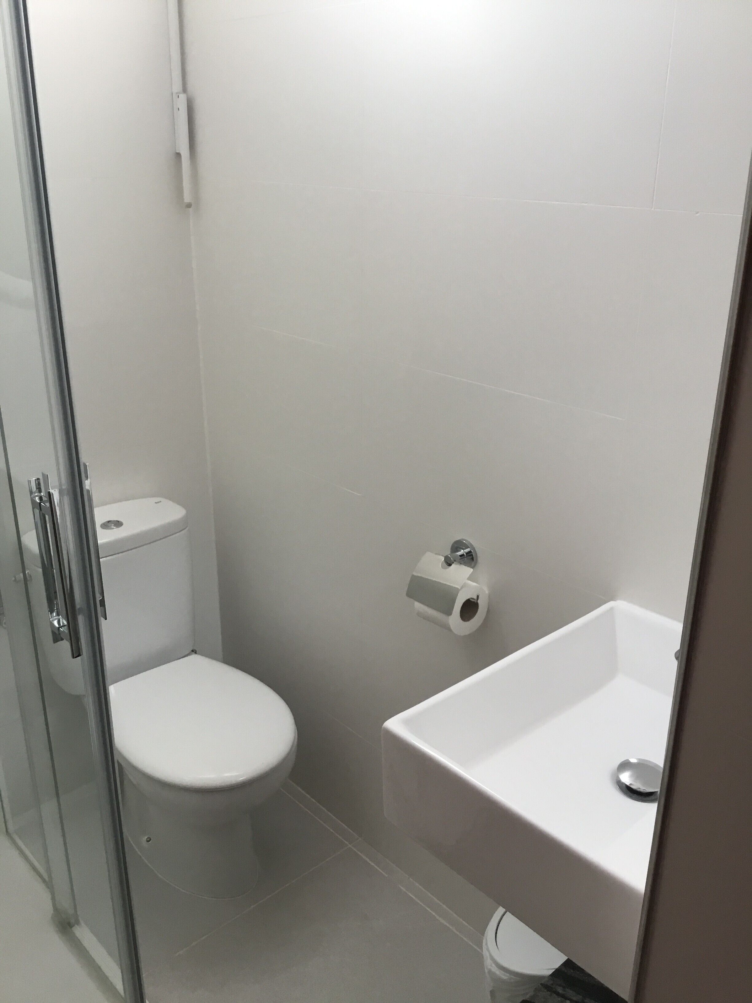A small, modern bathroom with a toilet, sink, and glass shower enclosure.