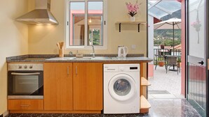 Une cuisine compacte équipée d’un four, d’un lave-linge et d’une fenêtre donnant sur un balcon.