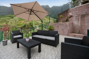 Un patio al aire libre con un sofá, sillas, una mesa y una sombrilla.