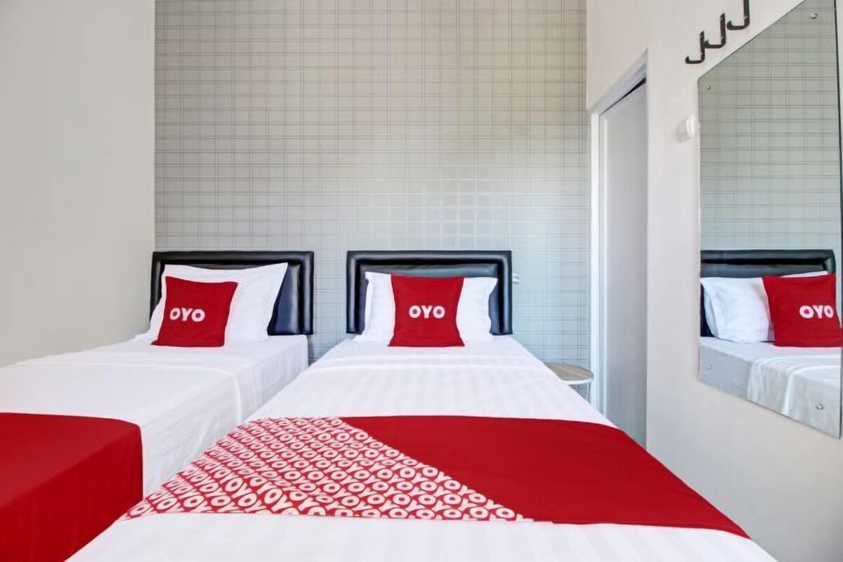 Een hotelkamer met twee bedden, elk voorzien van een rood-witte spreideken en kussens met de tekst 'OYO'.