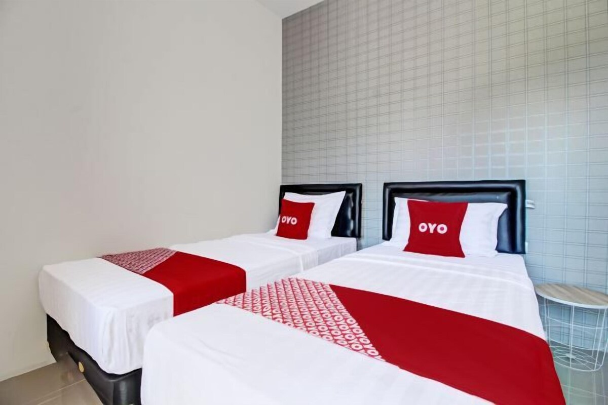 Habitación de hotel con dos camas, cada una con cubrecama y almohadas con la etiqueta 'OYO'.